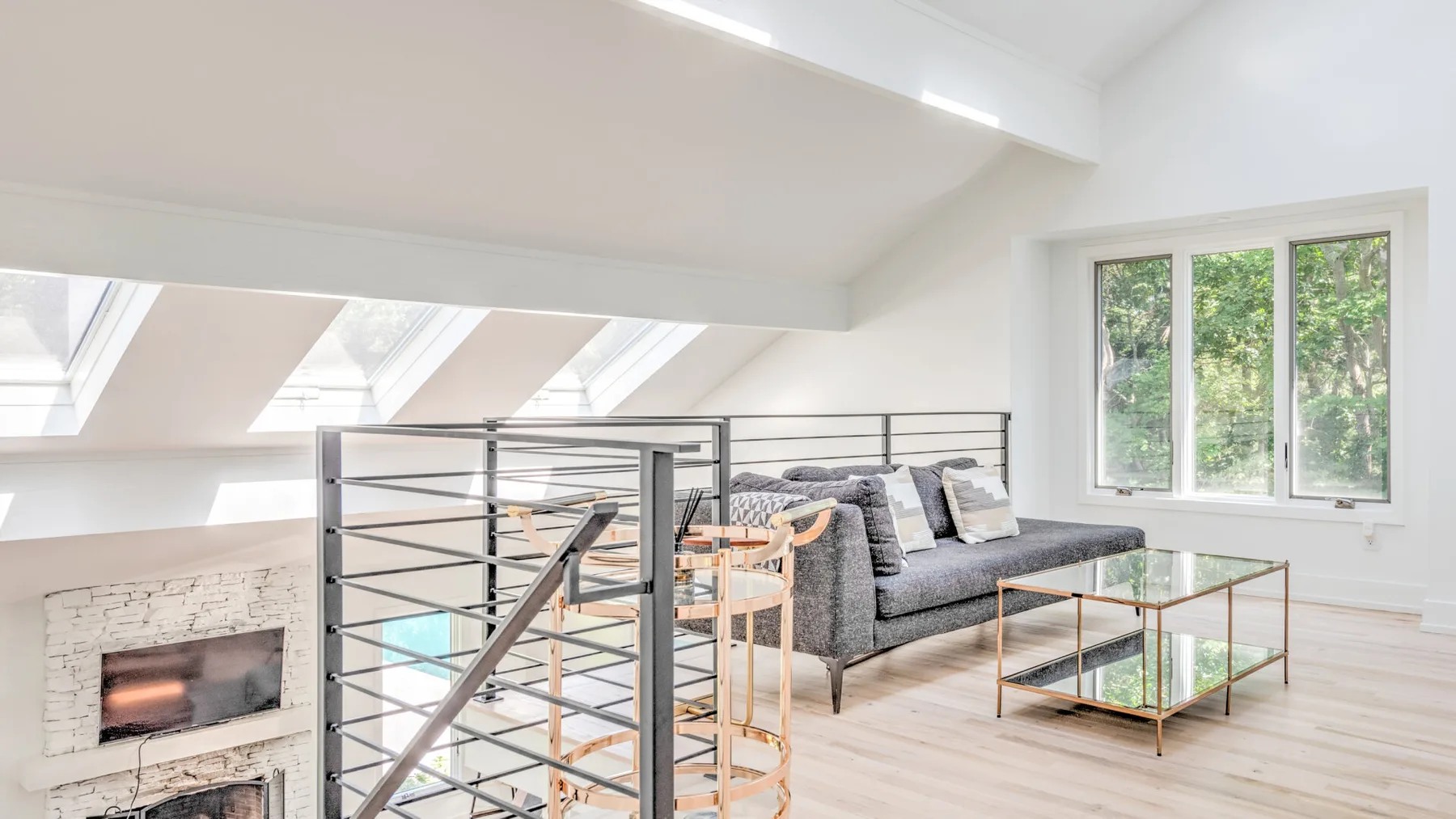 Una sala de estar luminosa con sofá gris, mesa de centro de vidrio y tragaluces.