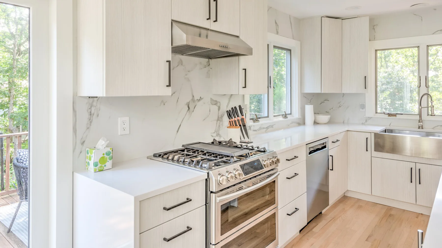 Una cocina luminosa con gabinetes blancos, encimeras jaspeadas y una estufa de acero inoxidable.