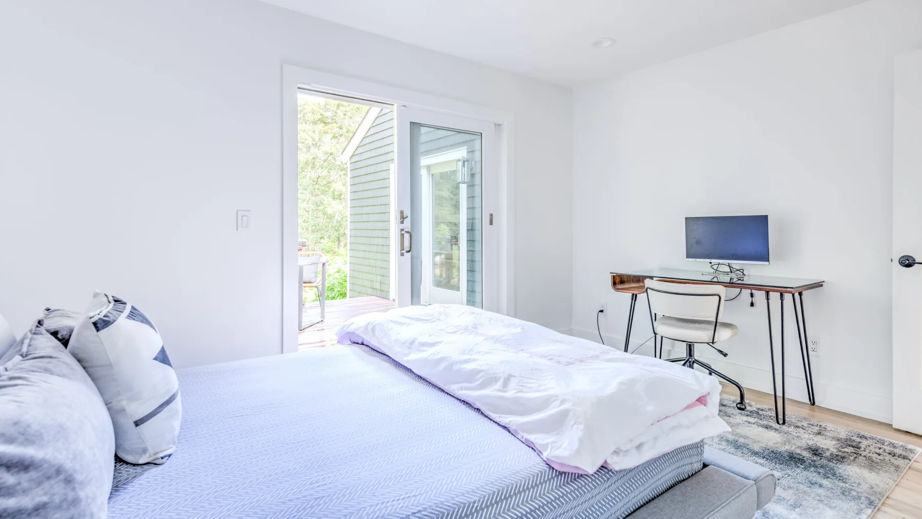 Un dormitorio luminoso con una cama junto a un escritorio y puertas de vidrio.