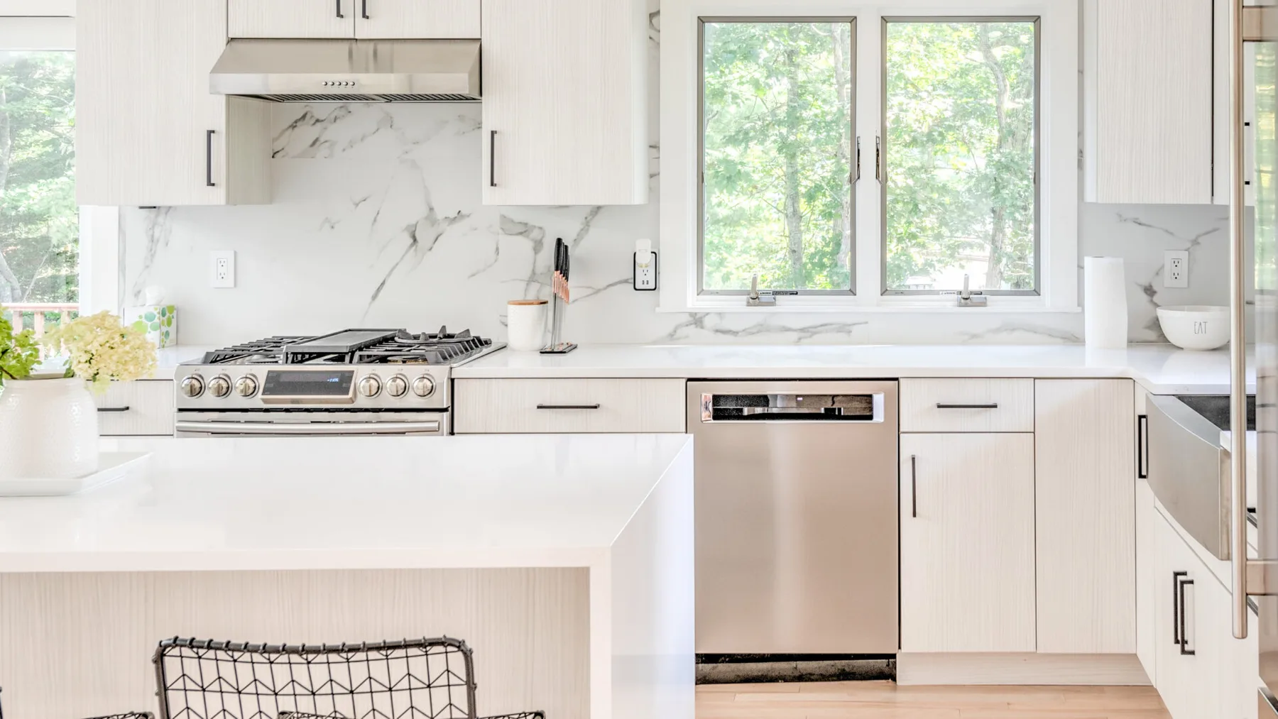 Una cocina luminosa con gabinetes blancos, una amplia isla y ventanas con vistas a la vegetación.