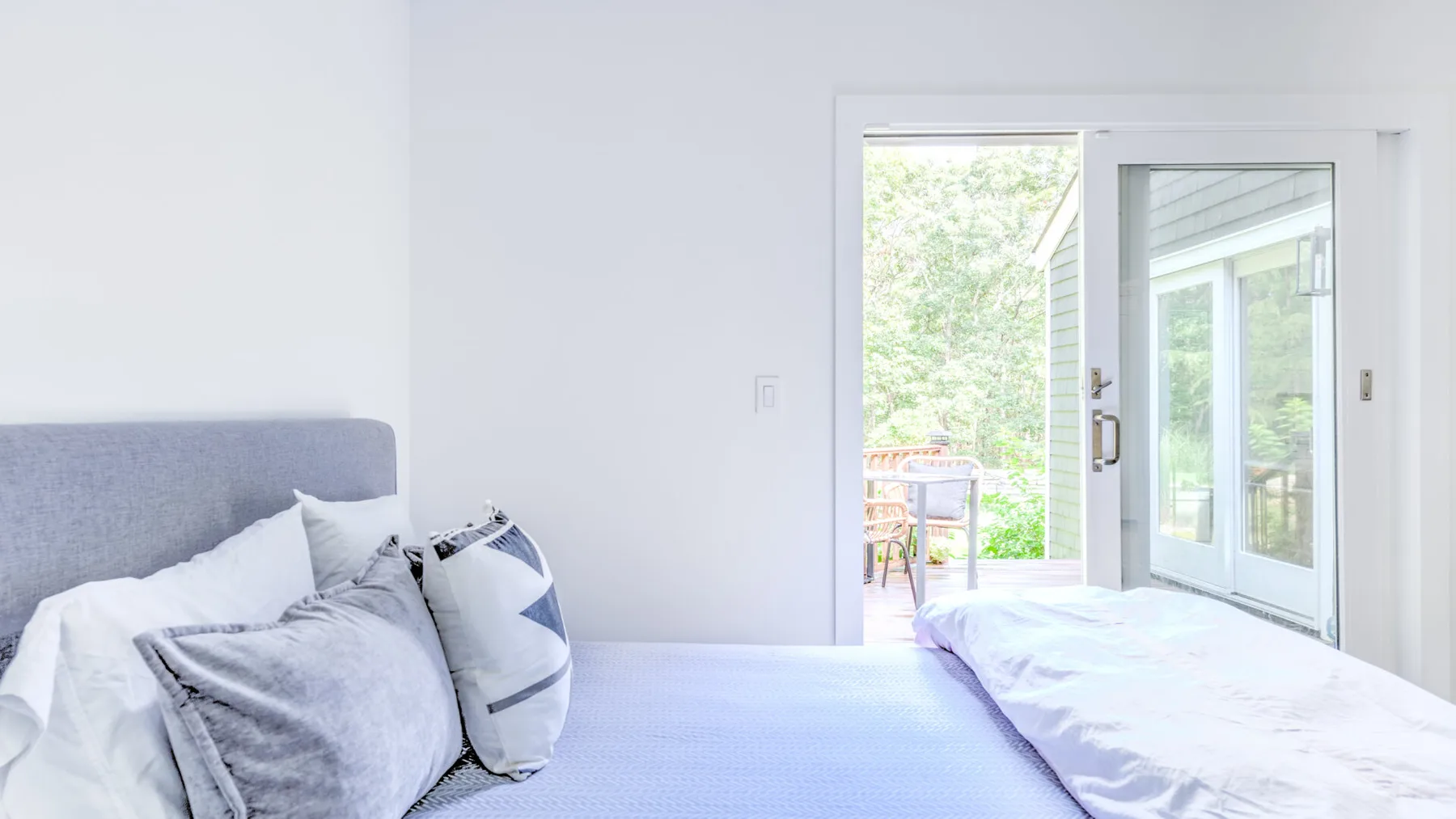 Un dormitorio luminoso con una cama junto a puertas de vidrio y vistas frondosas.