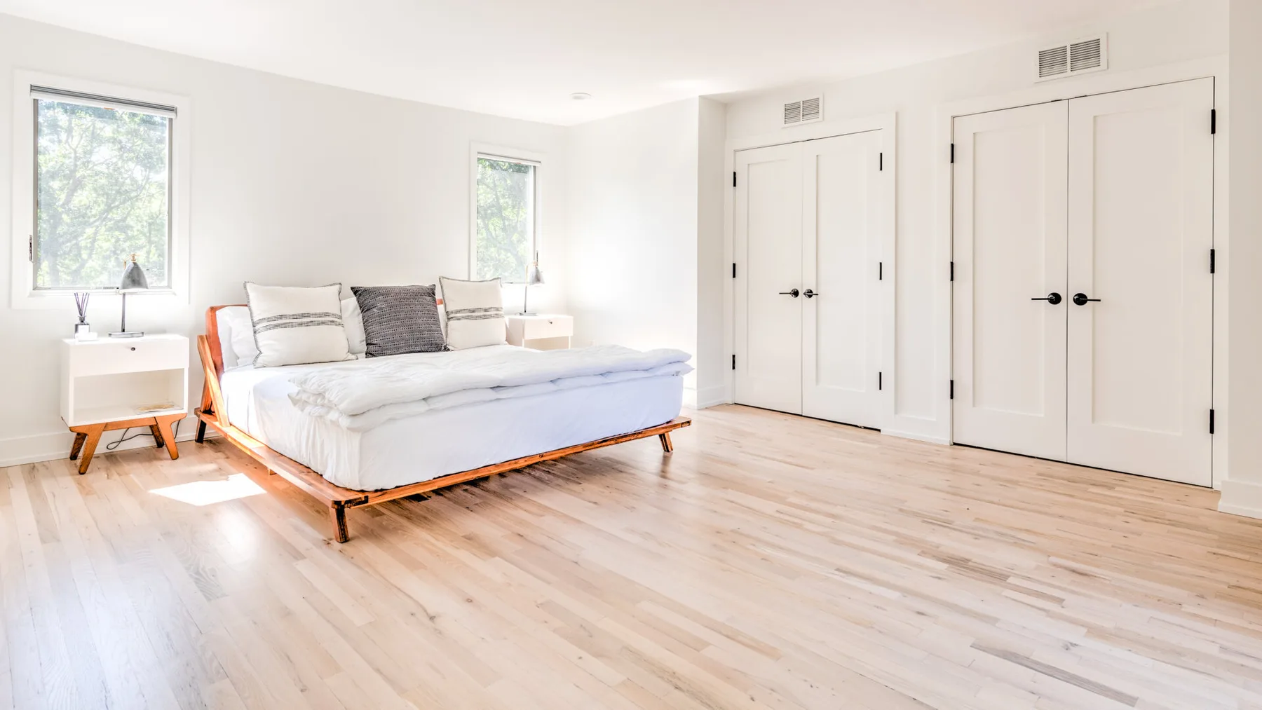 Un dormitorio luminoso con una cama baja, ropa de cama clara y suelo de madera clara.