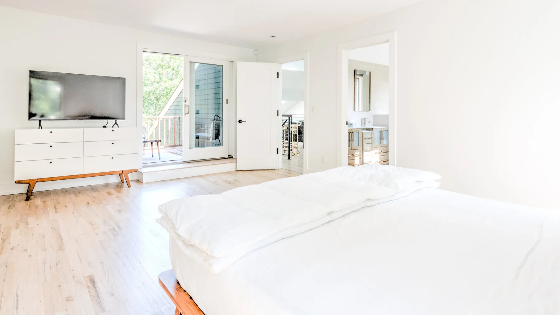 Un dormitorio luminoso con una cama, un televisor y puertas que dan a un balcón.