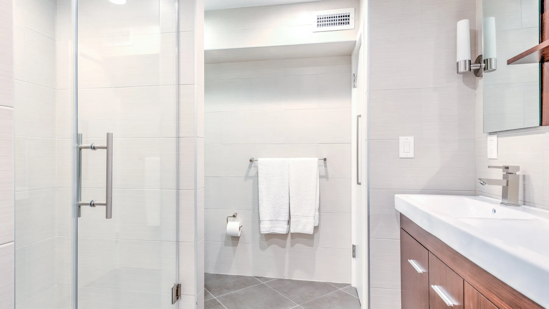 Un baño luminoso con azulejos, ducha de vidrio y lavabo con mueble.
