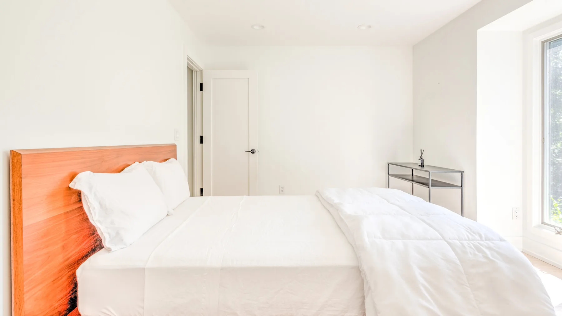 Un dormitorio luminoso con una cama, ropa de cama blanca y una ventana.