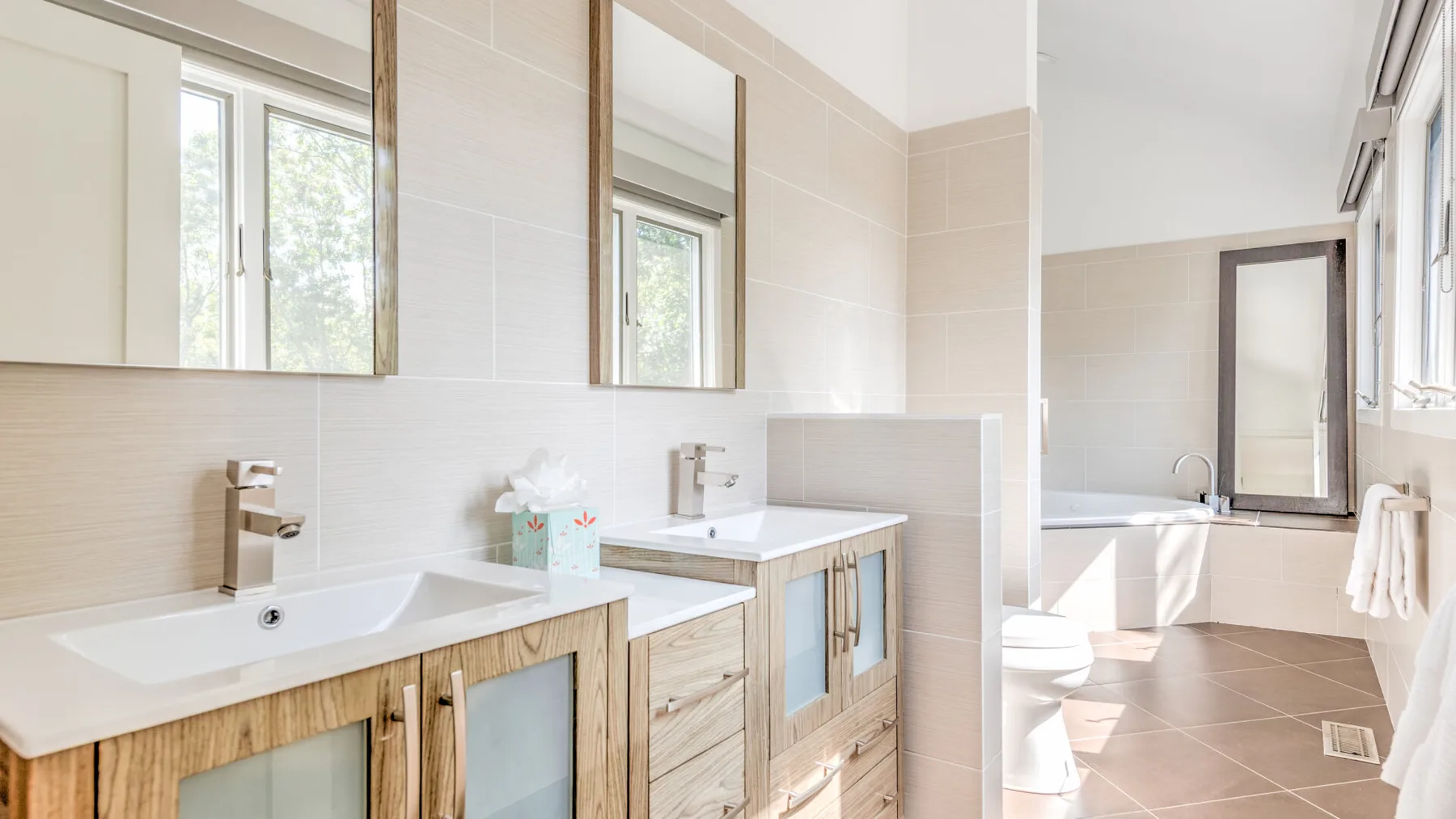 Un baño luminoso con lavabos dobles, una bañera y una ventana grande.