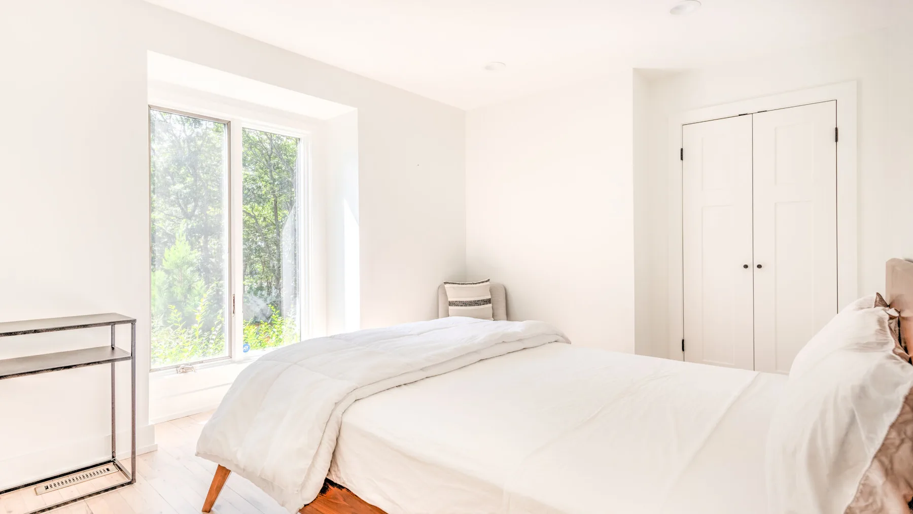 Un dormitorio luminoso con una cama tendida junto a una ventana grande.