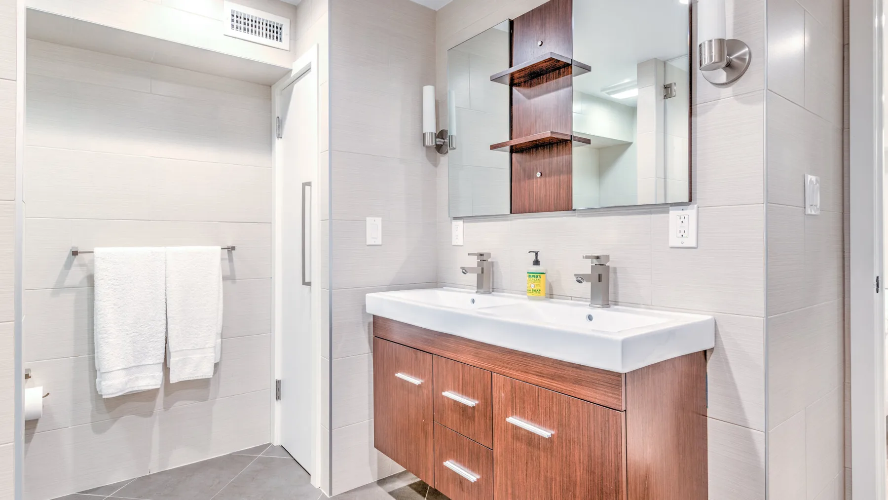 Un baño con lavabo doble, armario con espejo y toallero.