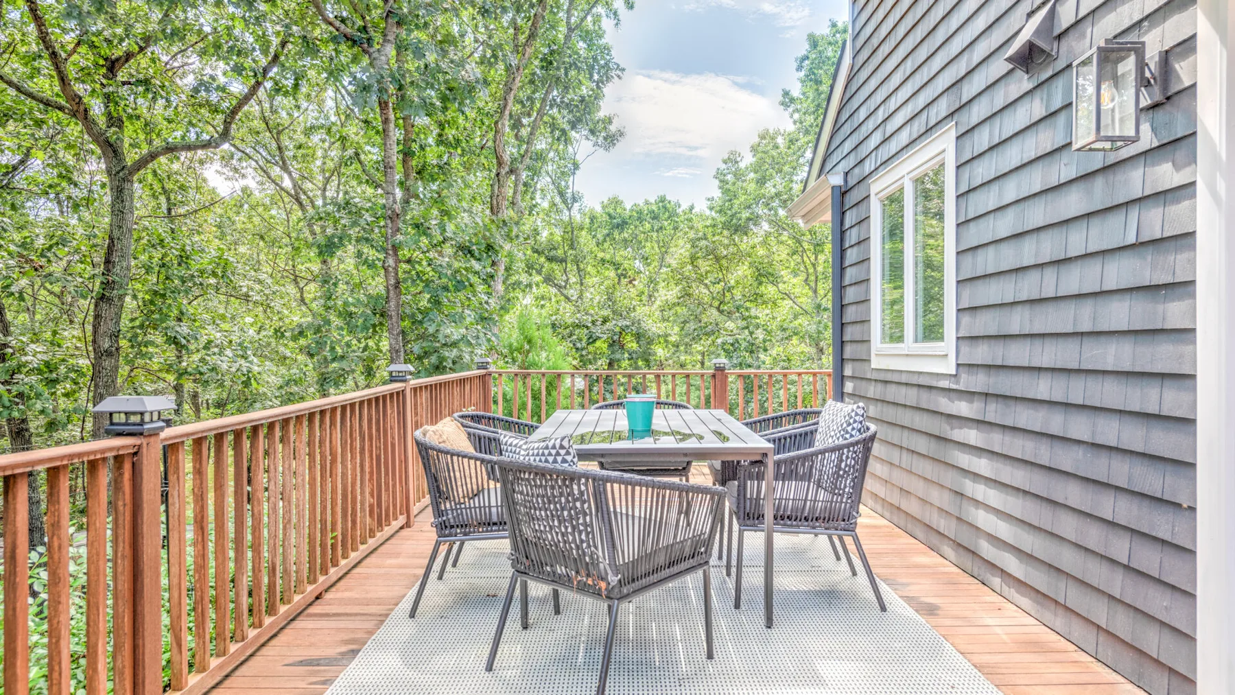 Una terraza exterior con mesa de comedor y asientos rodeada de árboles.