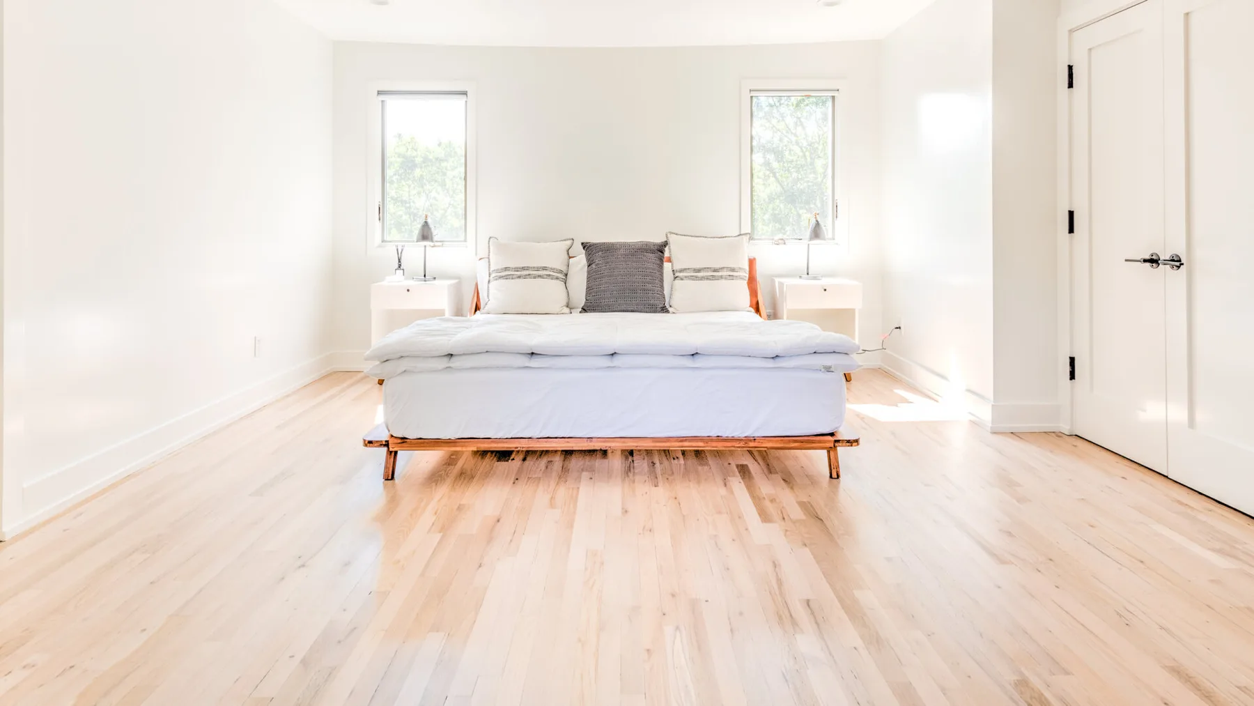 Un dormitorio luminoso con una cama entre dos ventanas.