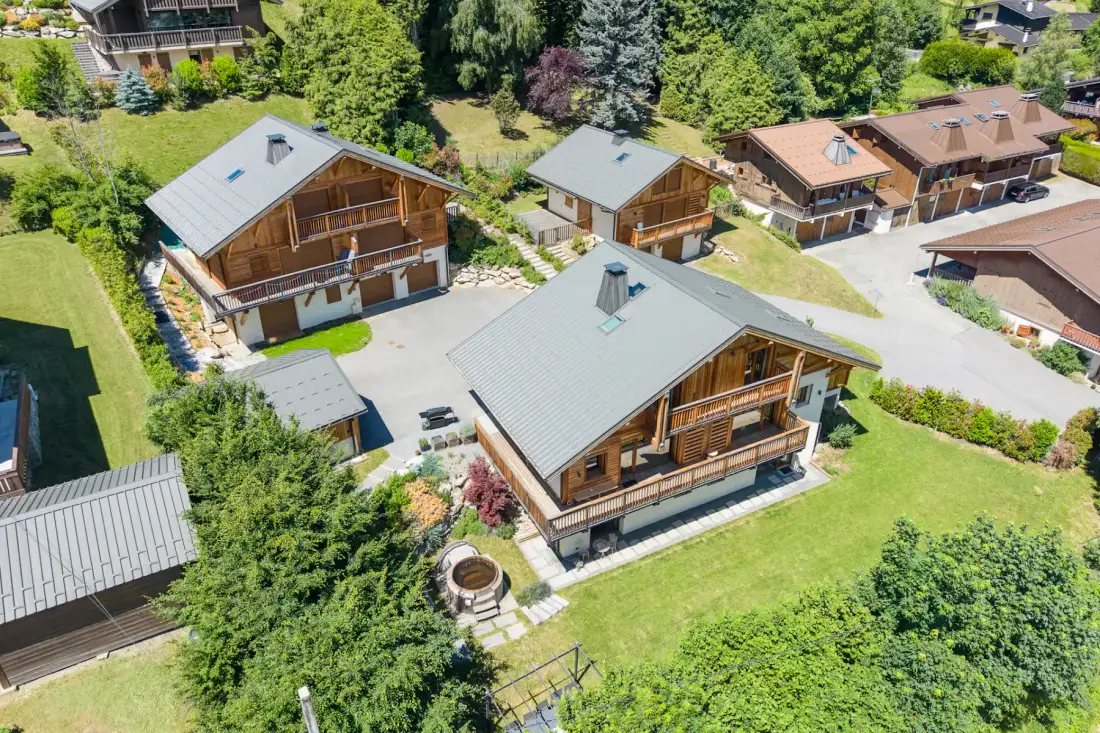 Aerial view of several chalets among green lawns and trees.