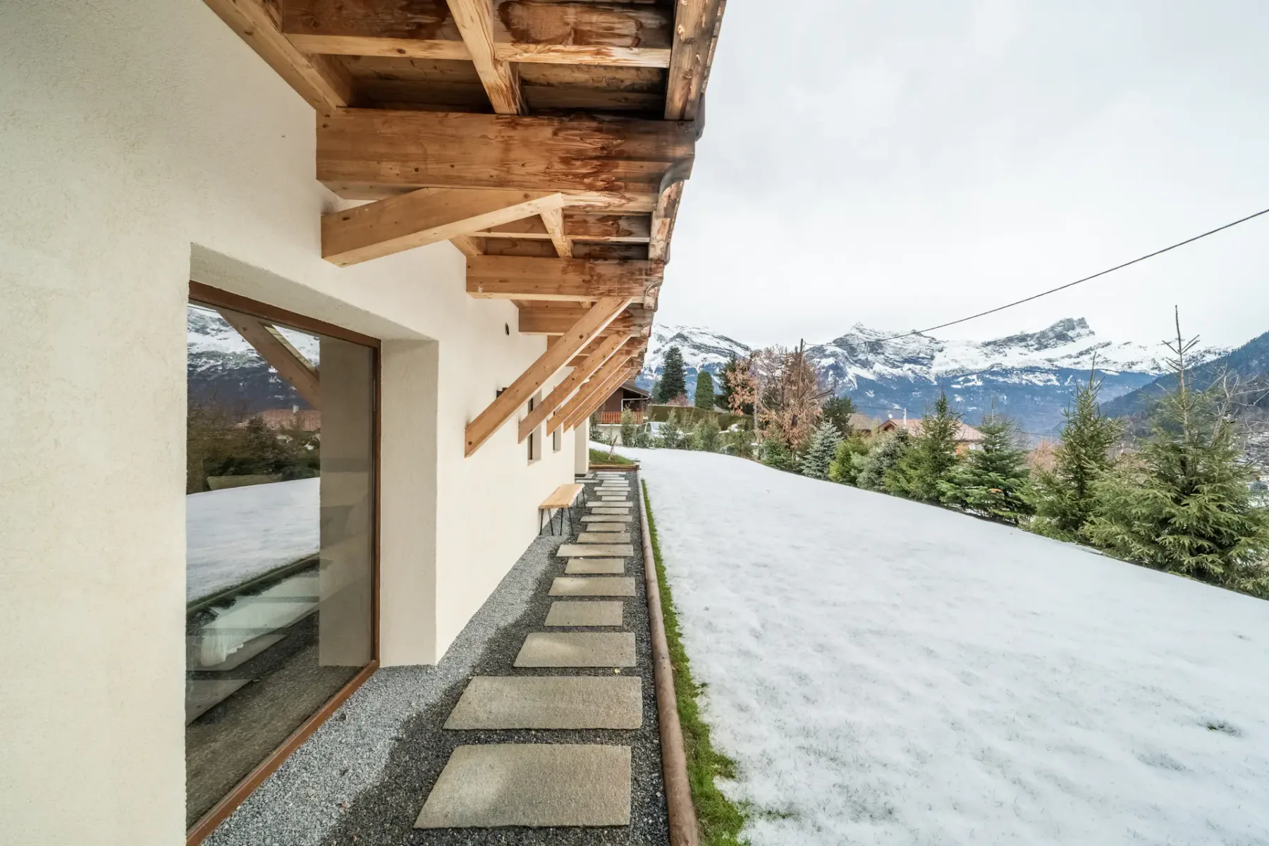 A snowy outdoor walkway runs beside a building, with mountain views beyond.