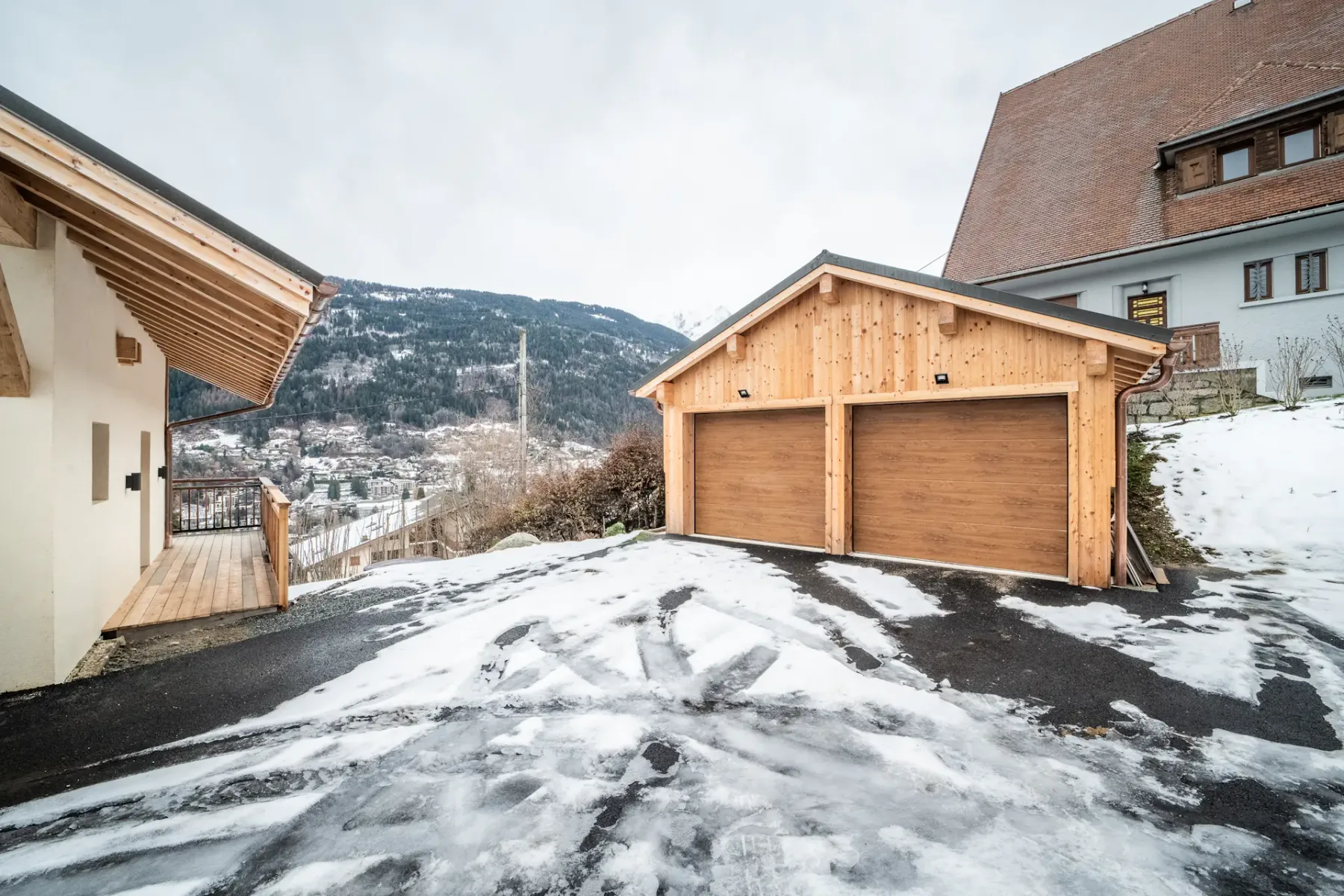 Snow-dusted driveway between a house and a wooden garage.