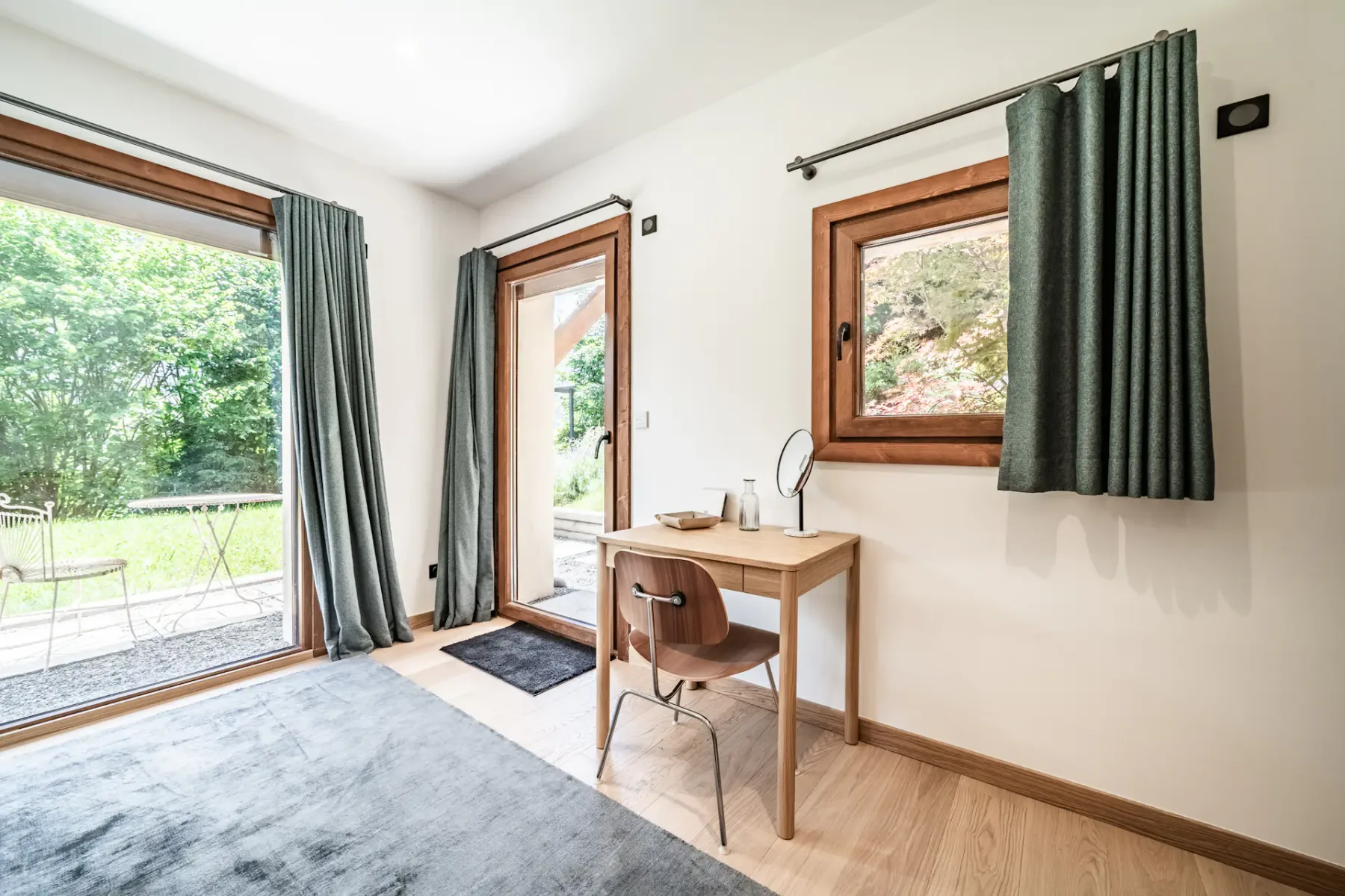 A bright bedroom with a desk and windows overlooking greenery.
