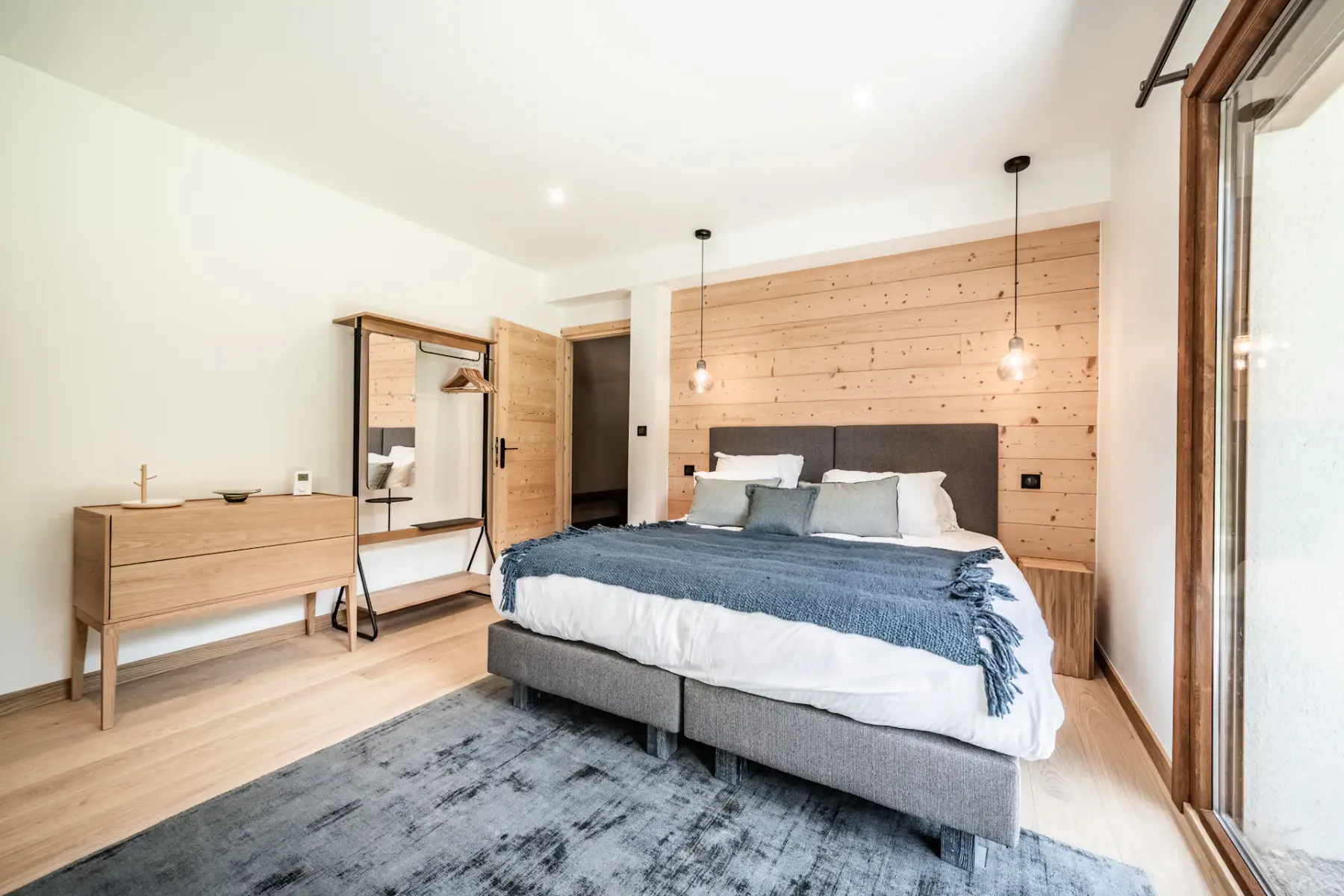A bedroom with a bed, wooden wall paneling, and a dresser.