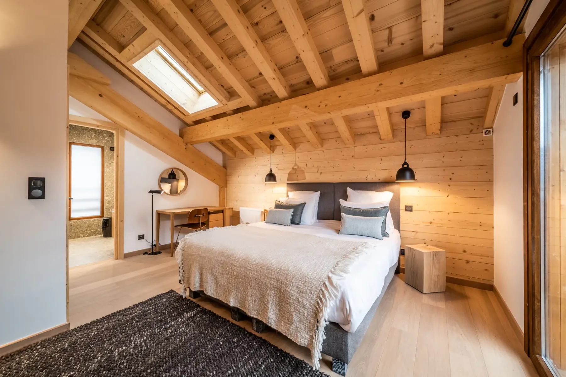 A bedroom with a double bed beneath a sloped timber ceiling.