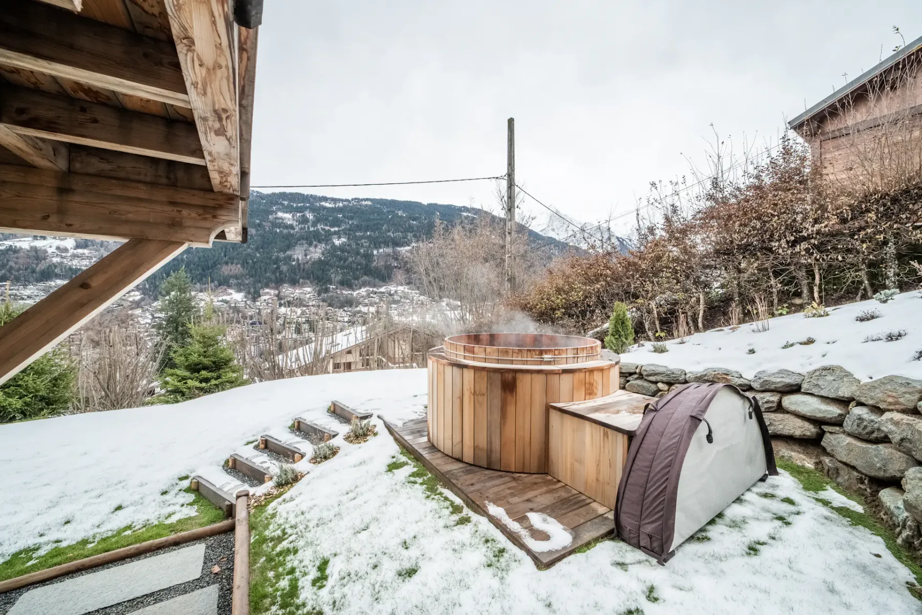 A snowy outdoor area with a wooden hot tub and mountain views.