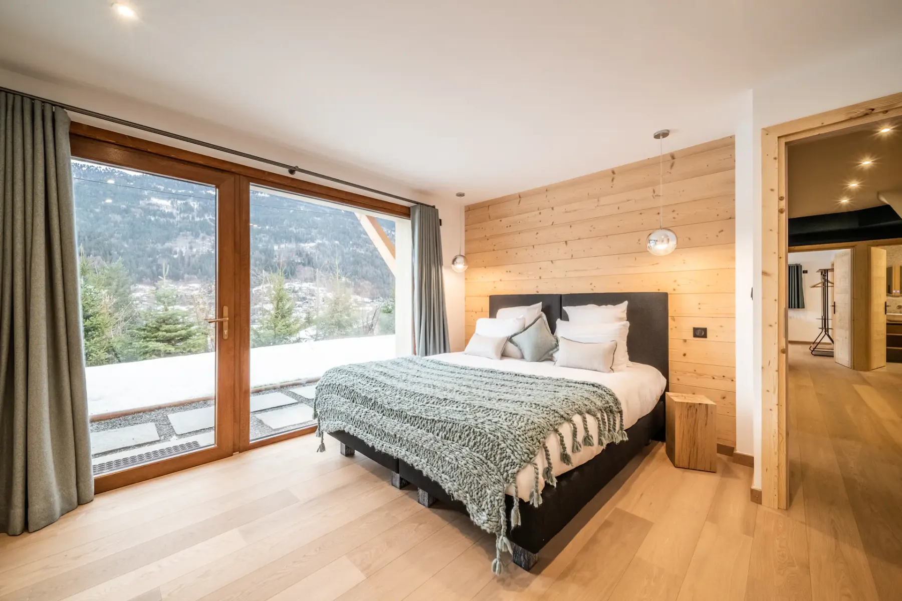A bedroom with a bed beside large windows overlooking a mountain landscape.