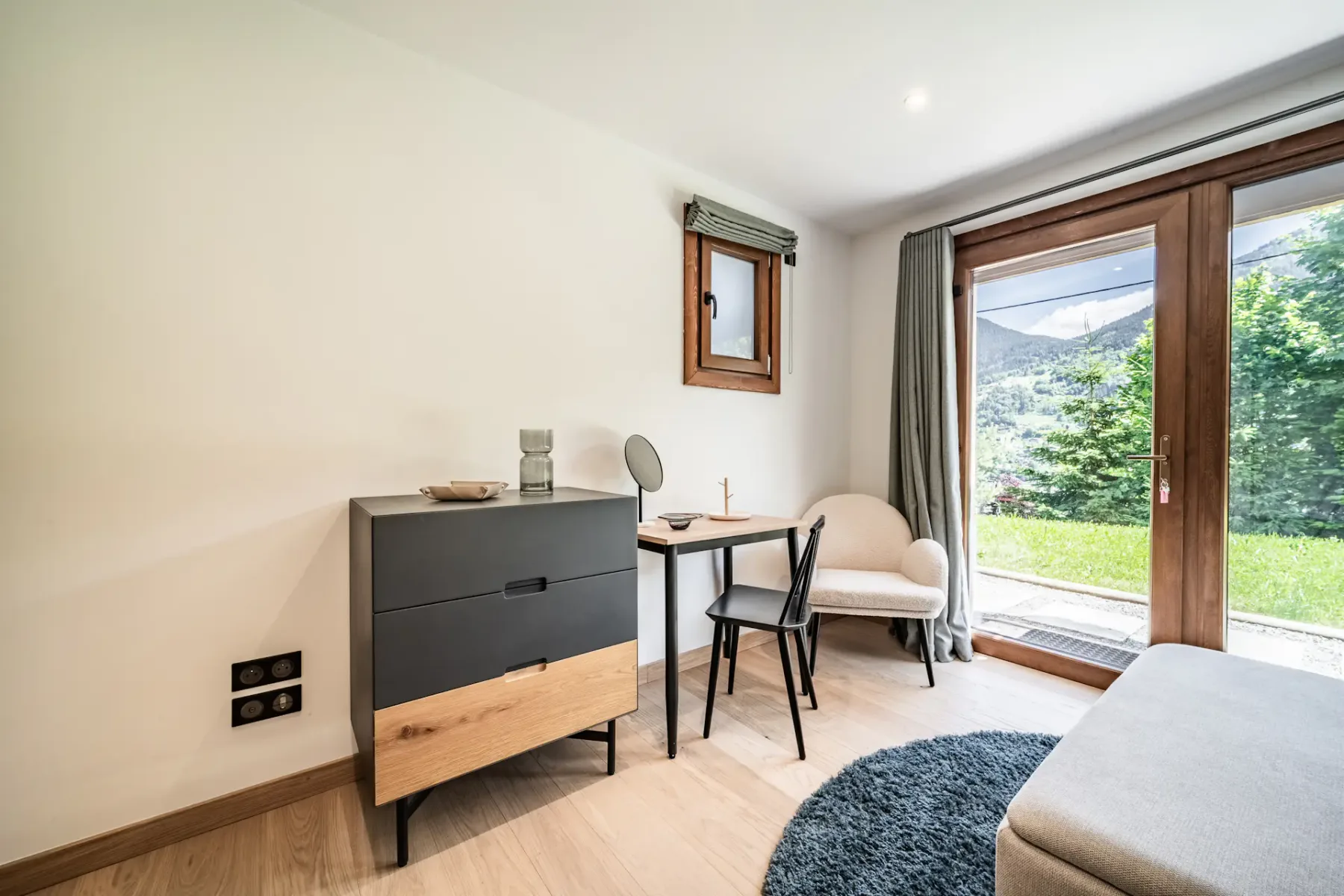 A bright sitting area with a dresser, small table, and large glass doors opening onto greenery.