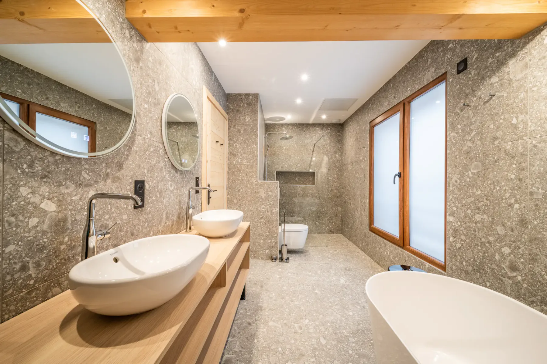 A spacious bathroom with stone-patterned walls, wooden vanity, and a freestanding bathtub.