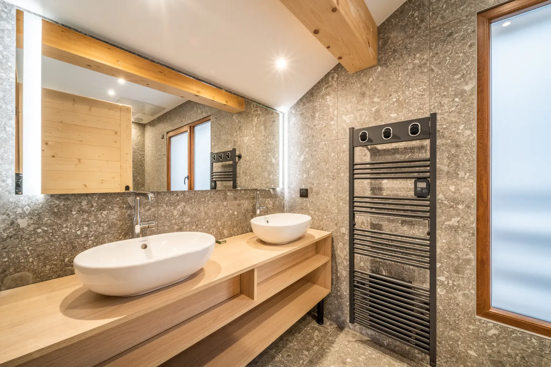 A bathroom vanity has two white vessel sinks beside a tall heated towel rail.