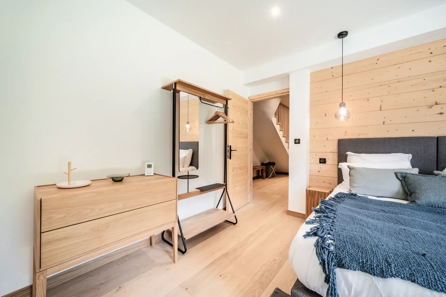 A bedroom with a bed, wooden dresser, and open wardrobe.