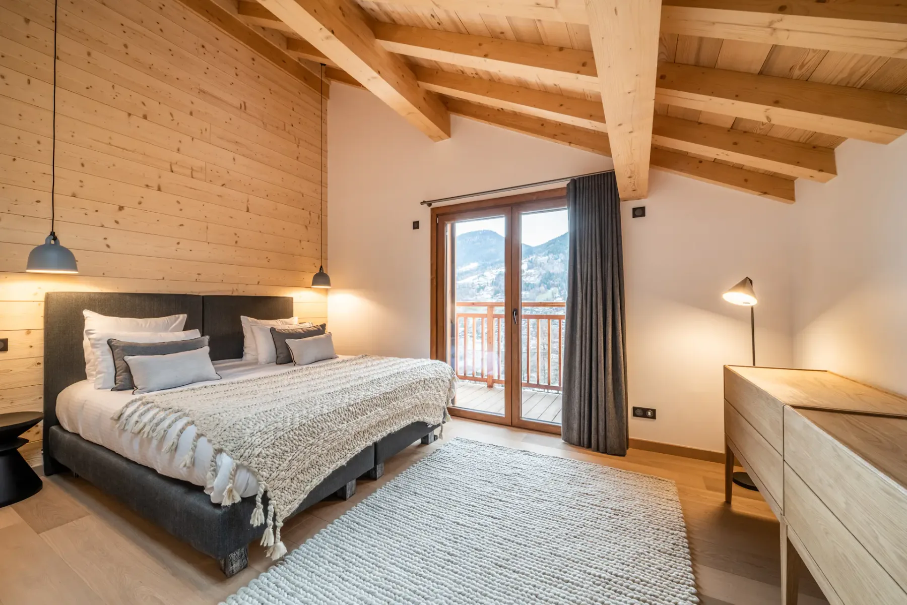 A bedroom with a bed, wooden ceiling beams, and a balcony door.