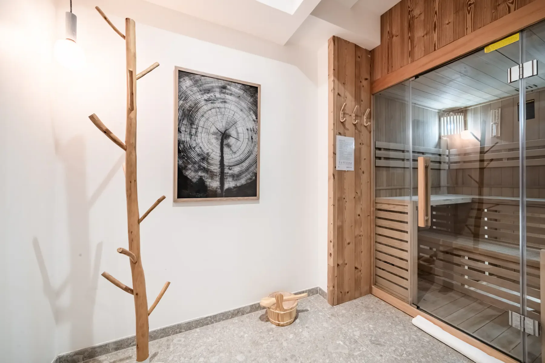 A sauna with wooden slats and a glass door sits beside a bright room.