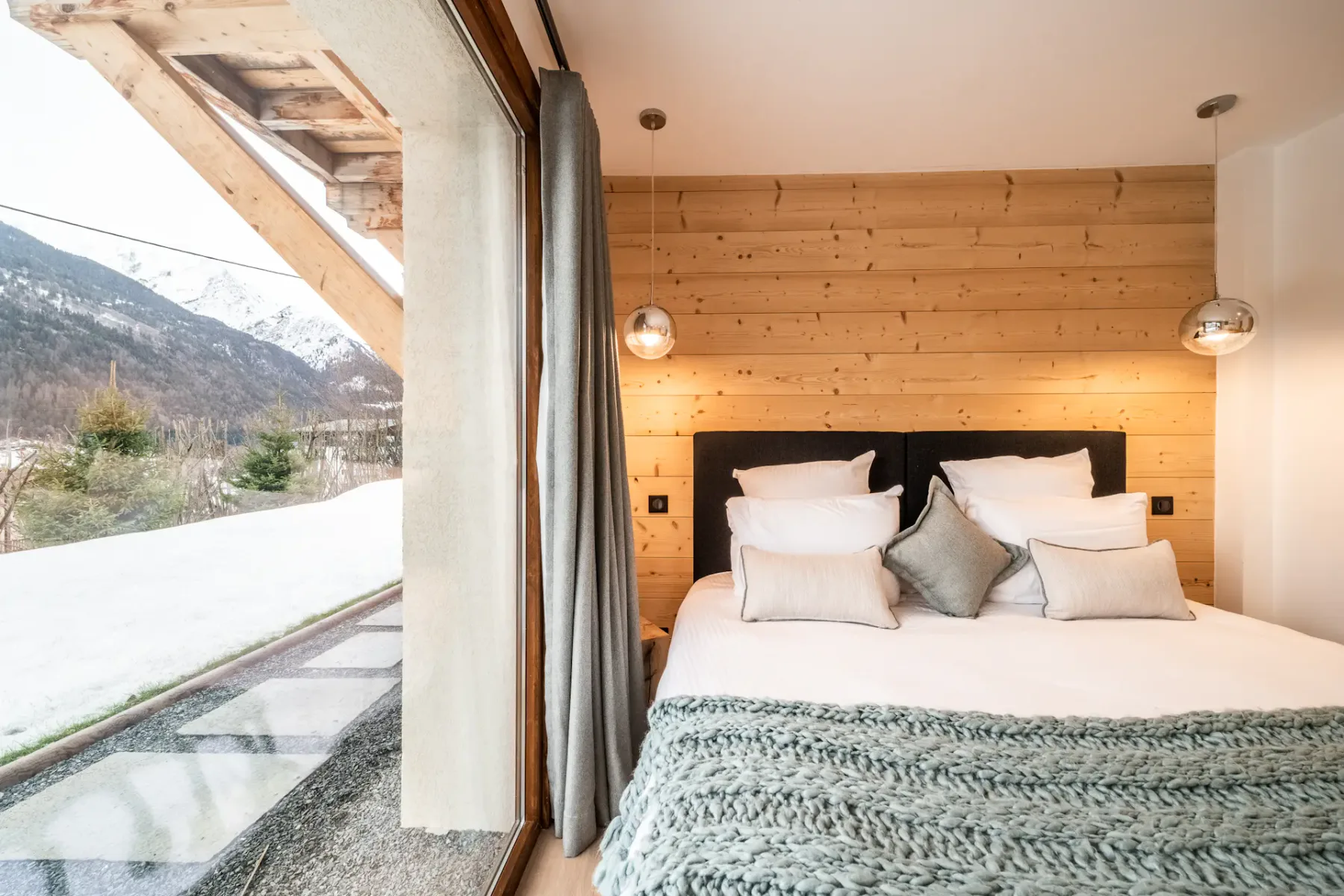 A bedroom with a bed beside a large window overlooking a snowy mountain landscape.