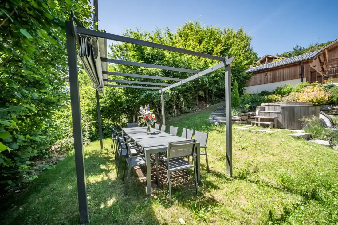 A garden dining area under a pergola, with a wooden table and chairs.