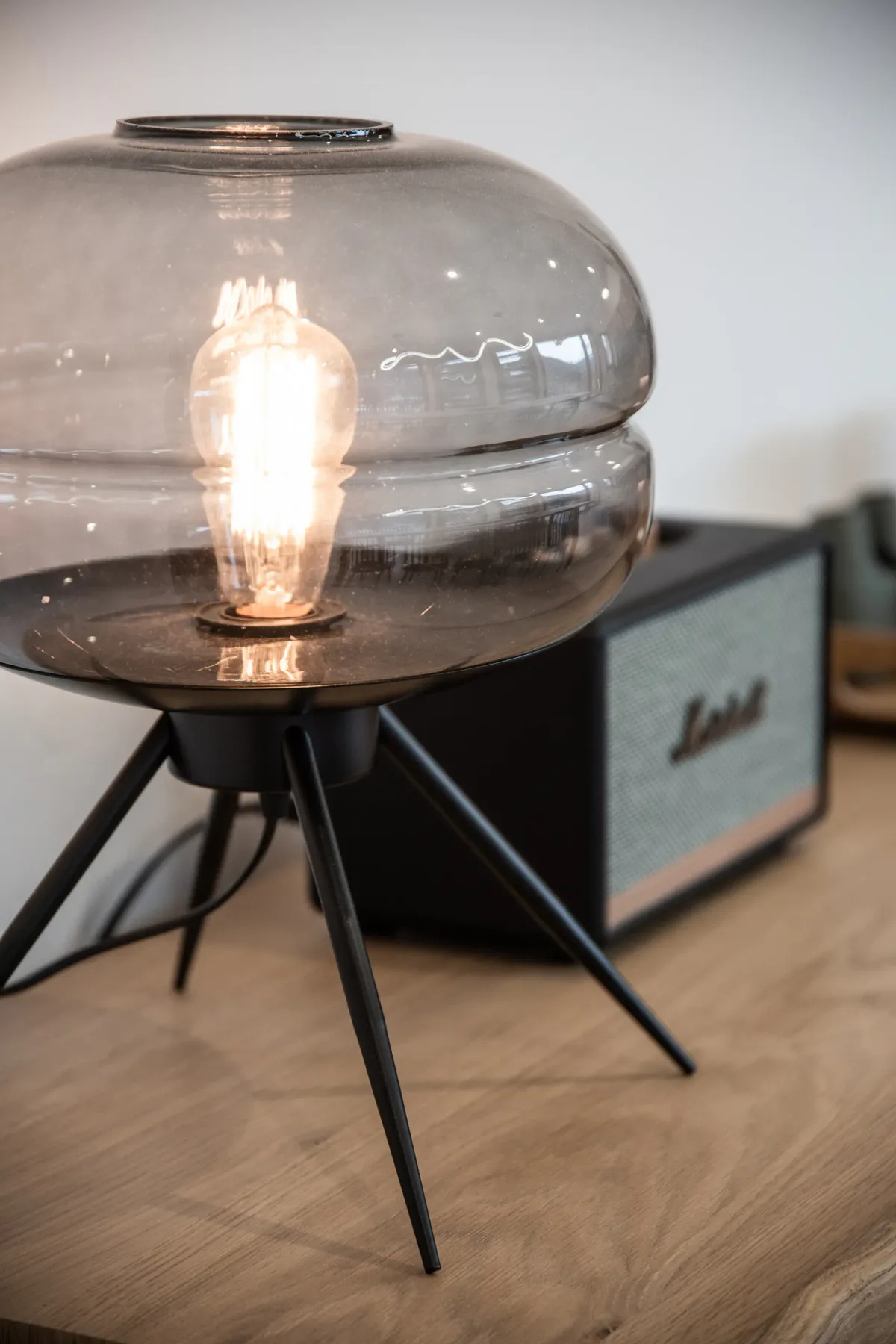 A glowing table lamp sits in front of a speaker on a wooden surface.