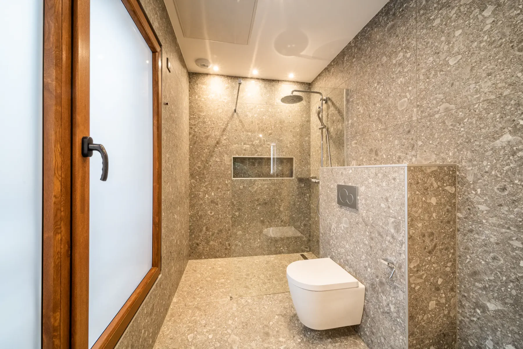 A stone-finished bathroom with a shower and a frosted window.