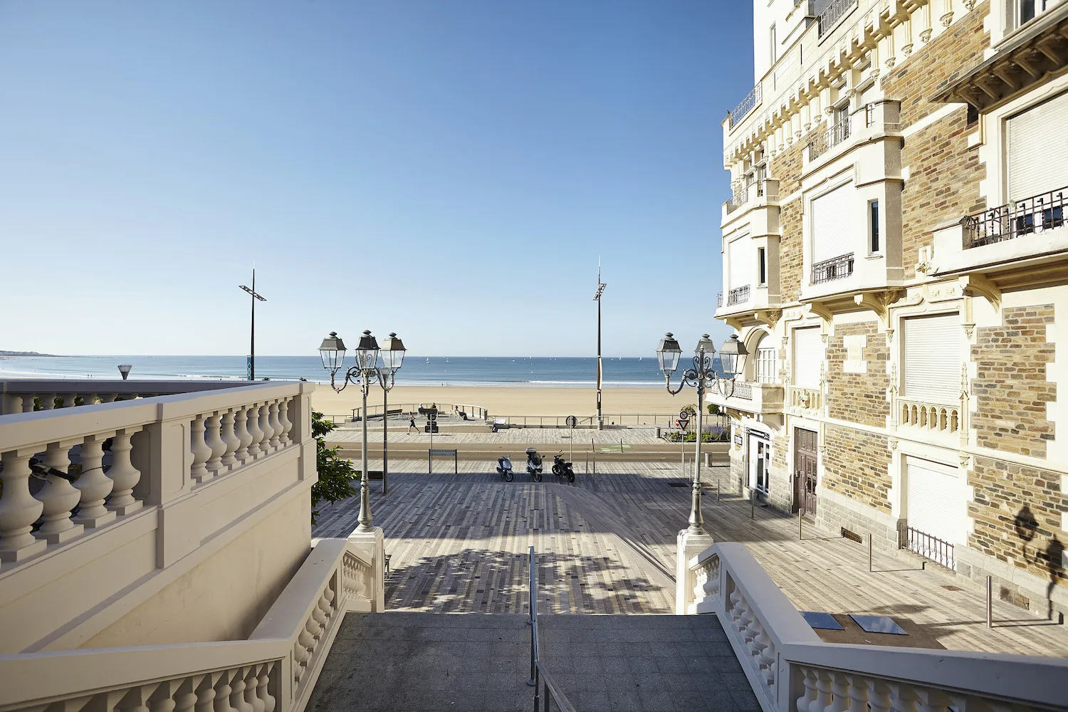 A seaside promenade and beach are visible beyond a broad outdoor terrace.