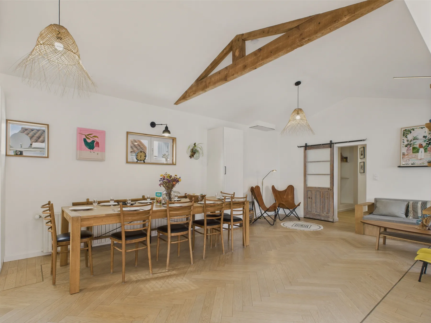 A bright dining area with a long wooden table beneath exposed ceiling beams.