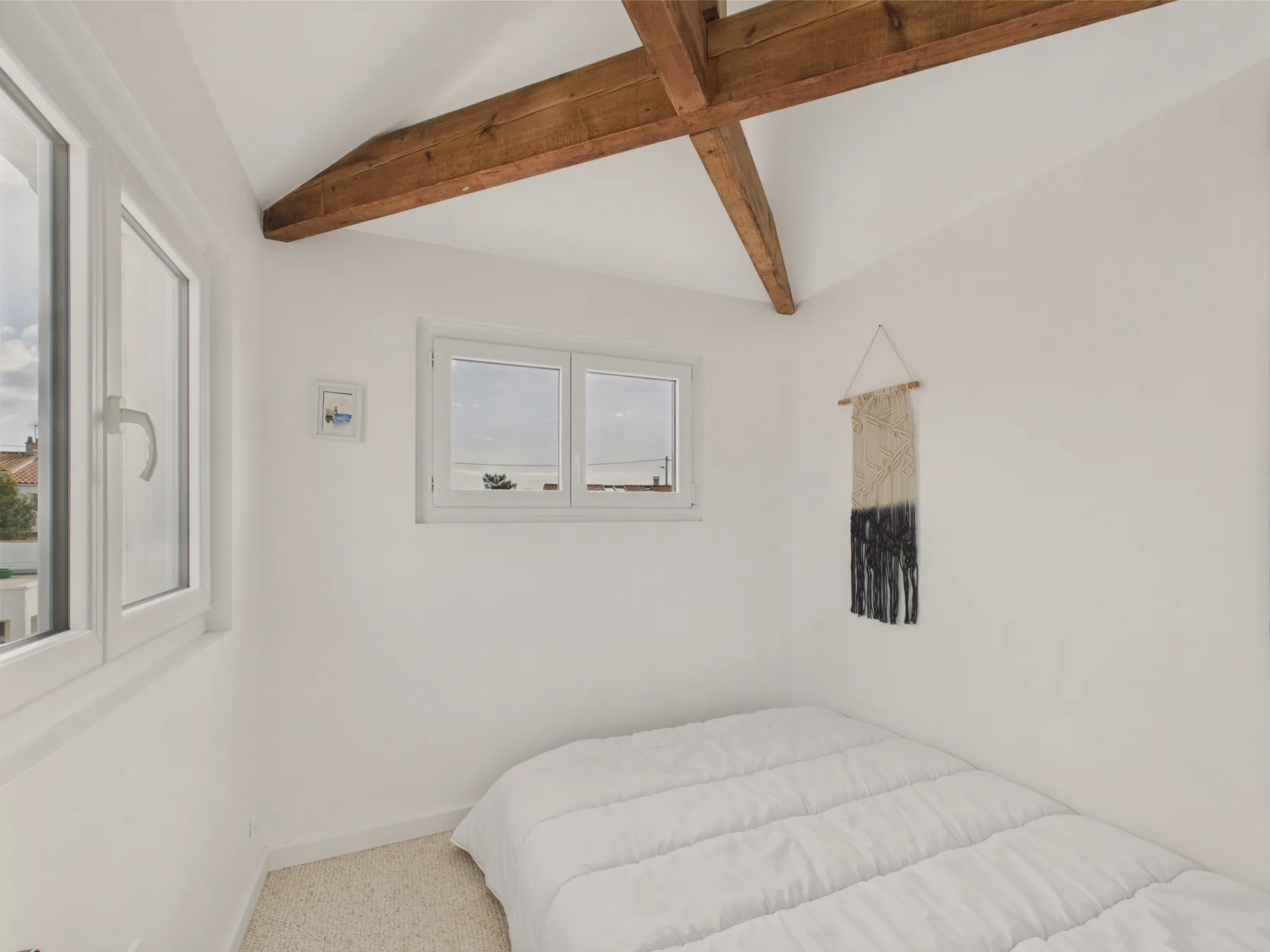 A bright bedroom with a bed beneath exposed wooden ceiling beams.