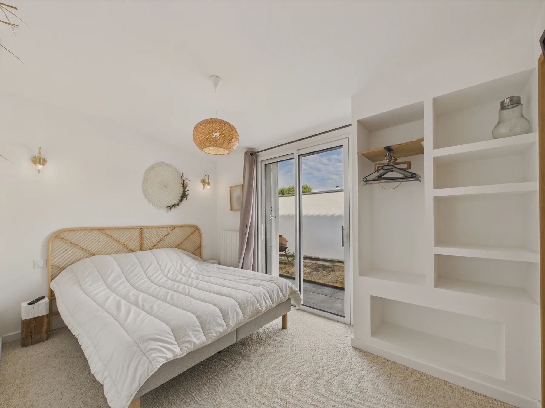 A bedroom with a bed beside a glass door and built-in shelving.