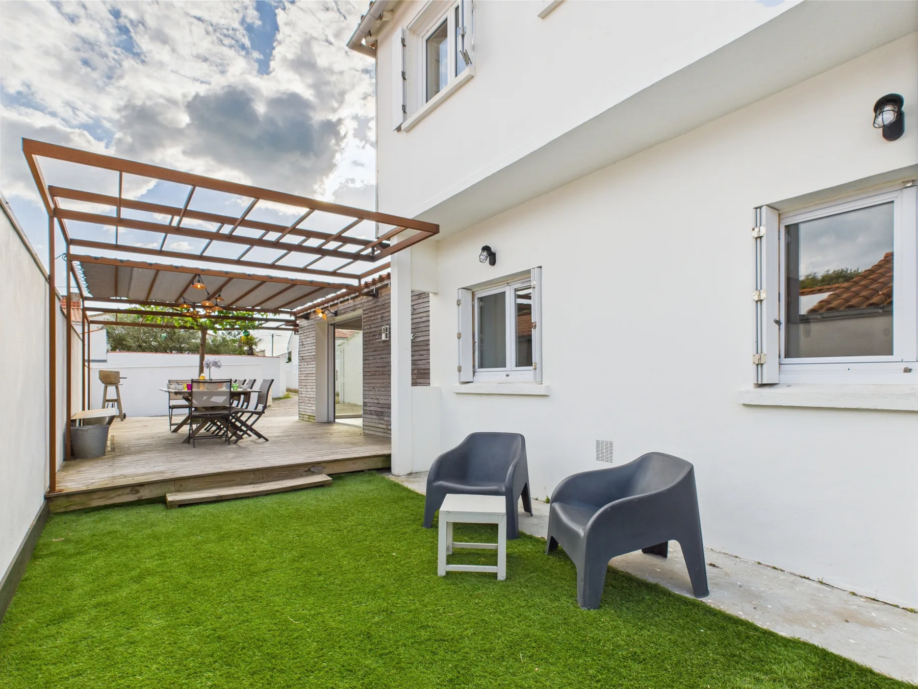 A grassy patio beside a white building, with seating under a pergola.