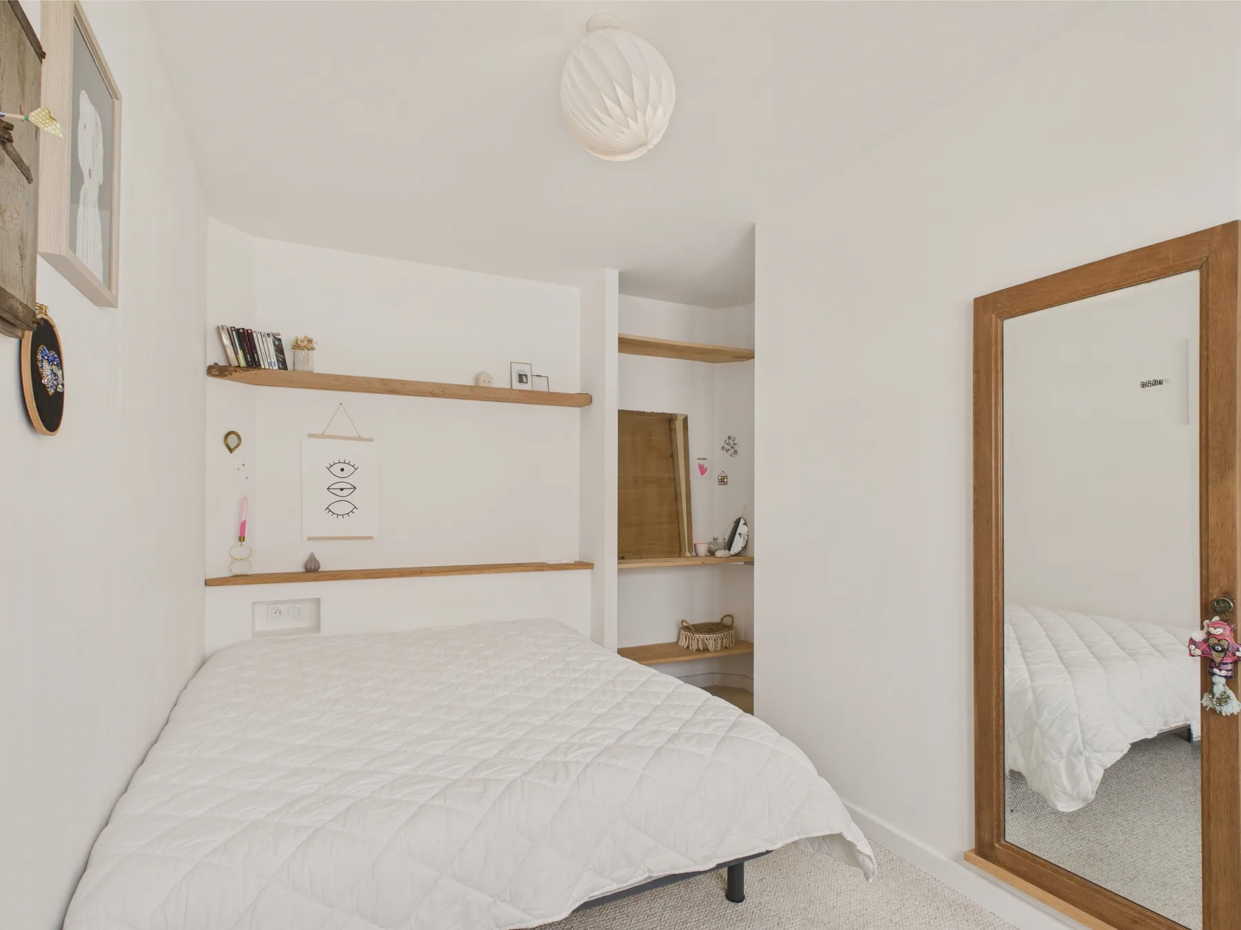 A bedroom with a neatly made bed and a full-length mirror.
