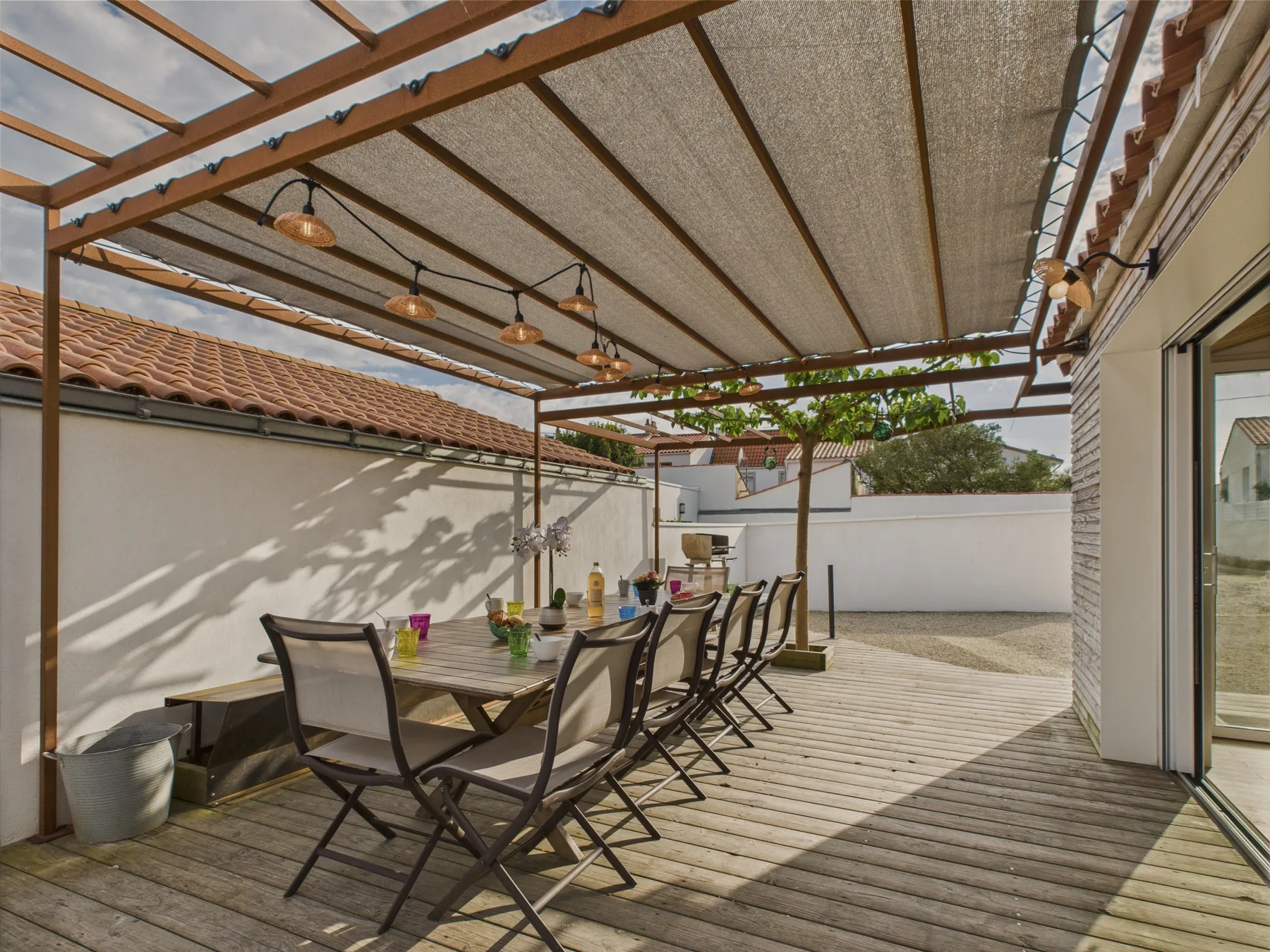 A covered outdoor dining area with a long table and chairs on a wooden deck.