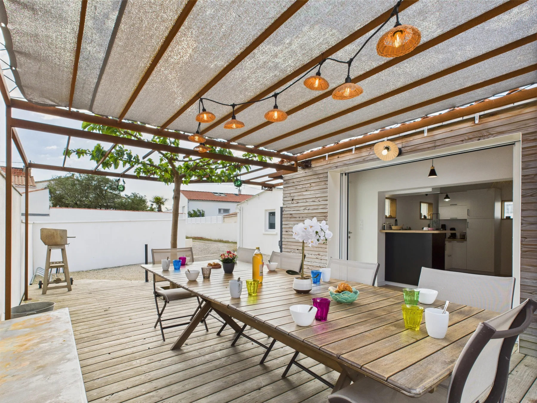 A covered outdoor dining area with a long table set with cups and dishes.