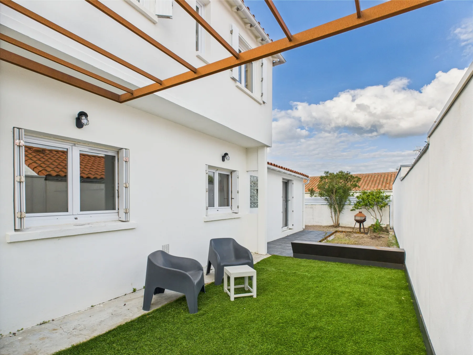 A small outdoor patio with green lawn, seating, and a wooden pergola.