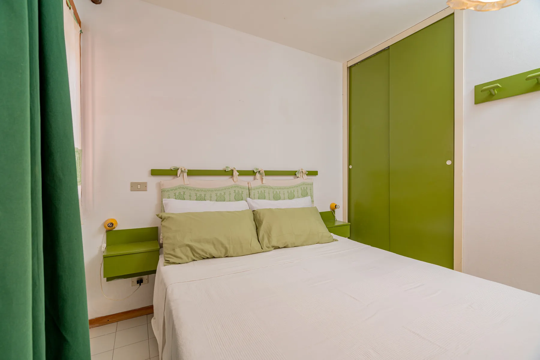 A bedroom with a bed, green curtains, and a matching wardrobe.