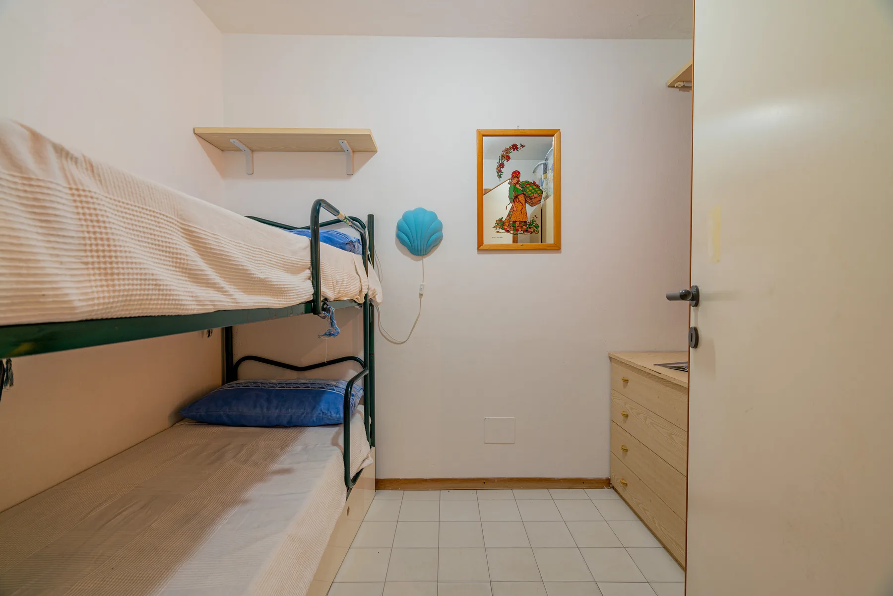 A small bedroom with bunk beds, a dresser, and a framed picture.