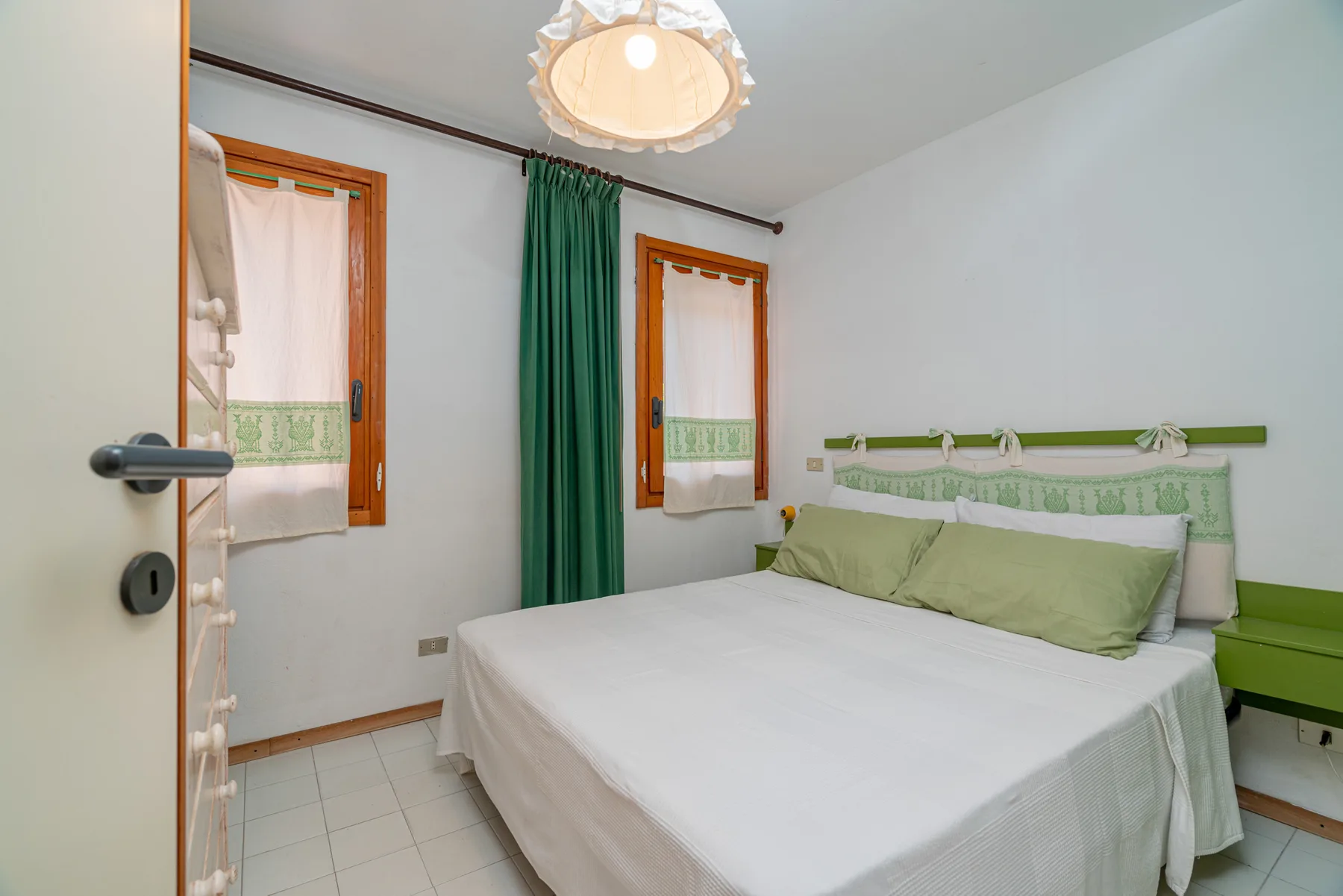 A bedroom with a bed, green curtains, and two windows.