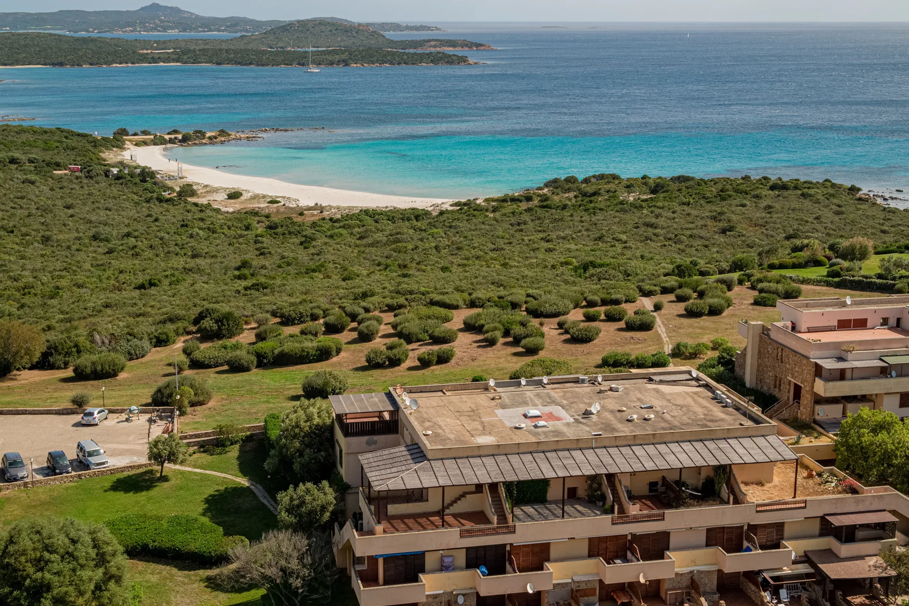 A coastal landscape with turquoise water, a sandy beach, and buildings in the foreground.