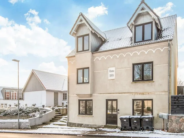 A pale multi-story house with dormer windows stands beside a snowy walkway.