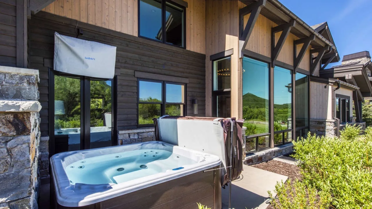 A hot tub sits beside a modern house with large windows and a mountain view.