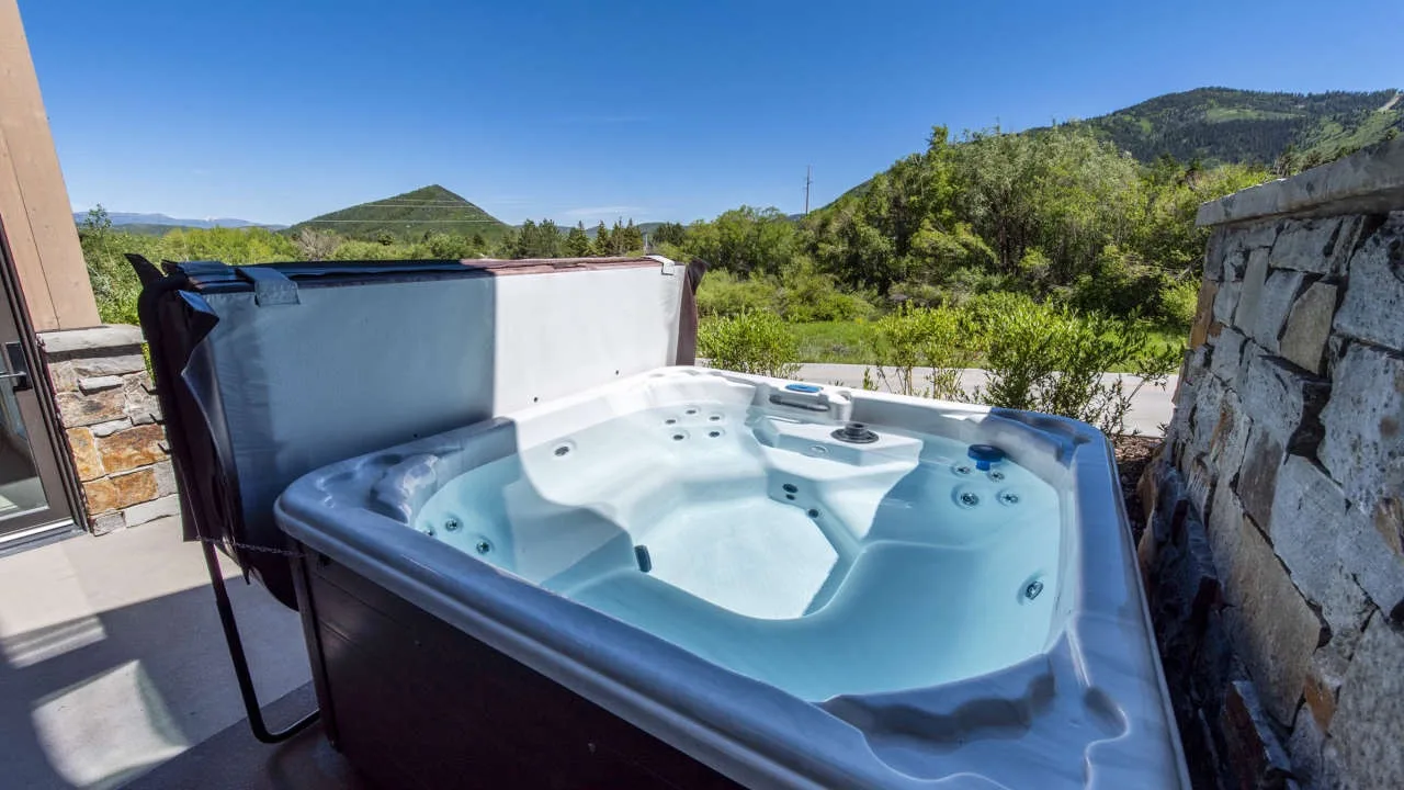 An outdoor hot tub sits beside a stone wall, with green hills in the background.