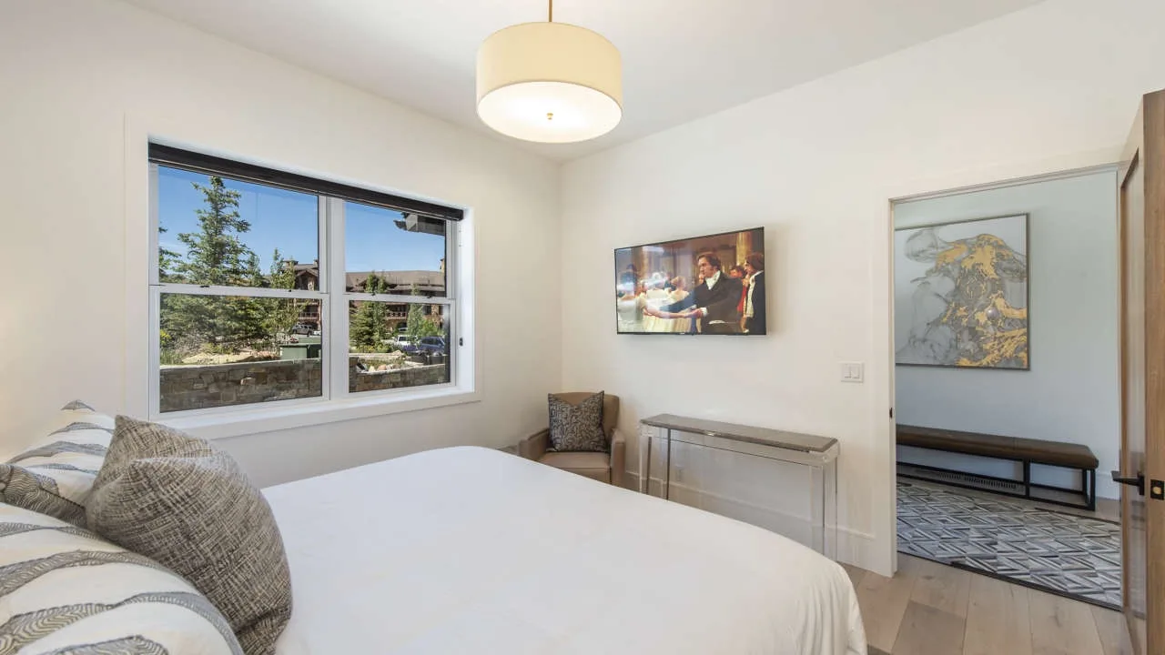 A bedroom with a bed, a window, and an open doorway to an adjoining room.