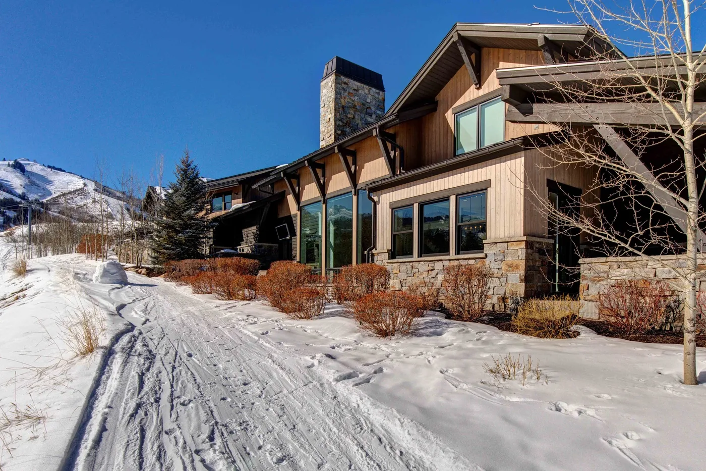 A large house stands beside a snow-covered path, with mountains visible in the distance.